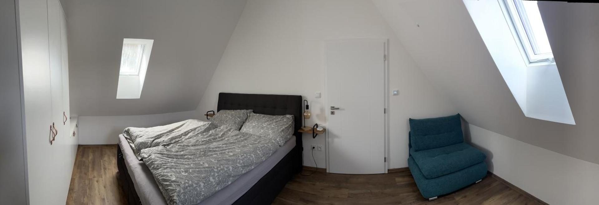 Ložnice pod šikmou střechou s manželskou postelí a křeslem